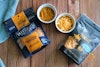 Miyoko's and Violife Cheddar cheese packages with each cheese in a ramekin, laying on a table.