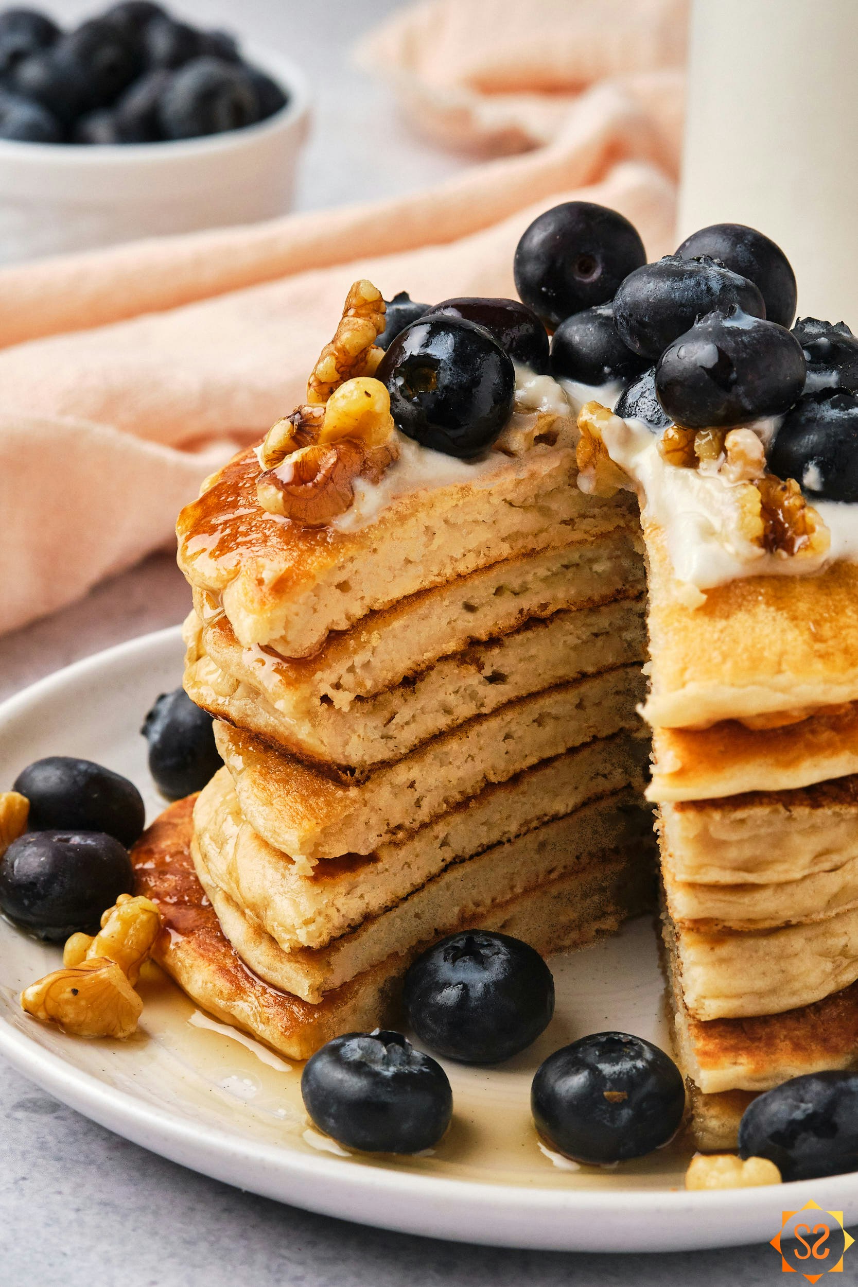A stack of vegan protein pancakes topped with blueberries and walnuts, with a slice cut out.