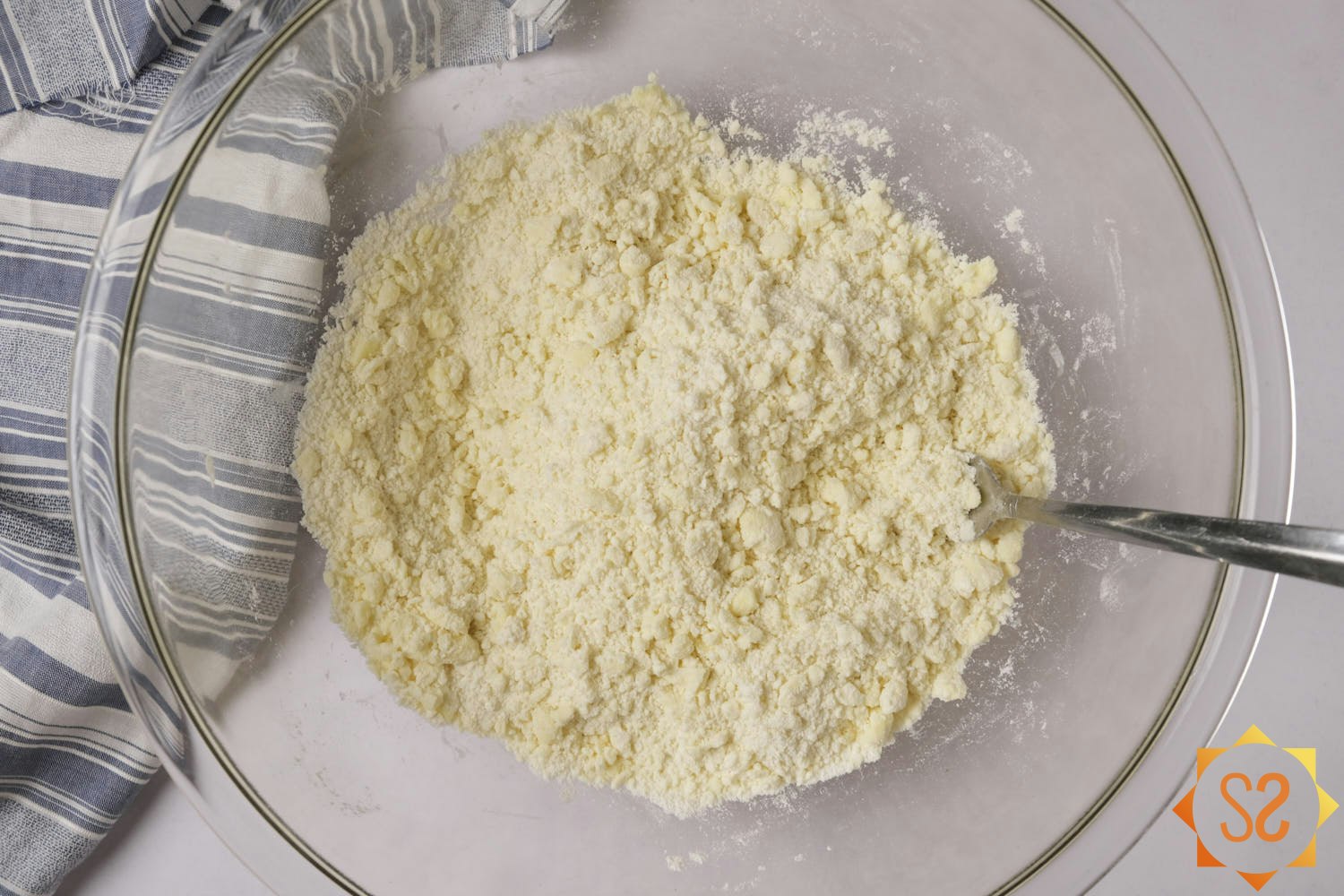 Dry ingredients in a mixing bowl with vegan butter cut in, producing a slightly lumpy mixture.