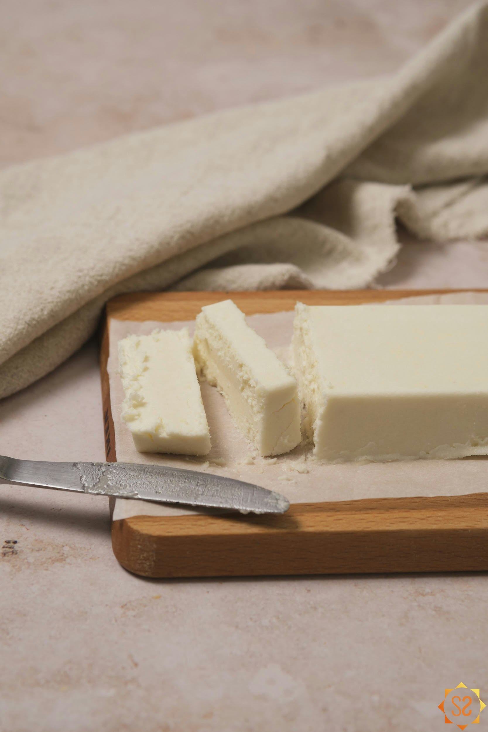 A block of vegan butter on a wooden slab, sliced, with a knife to the side.