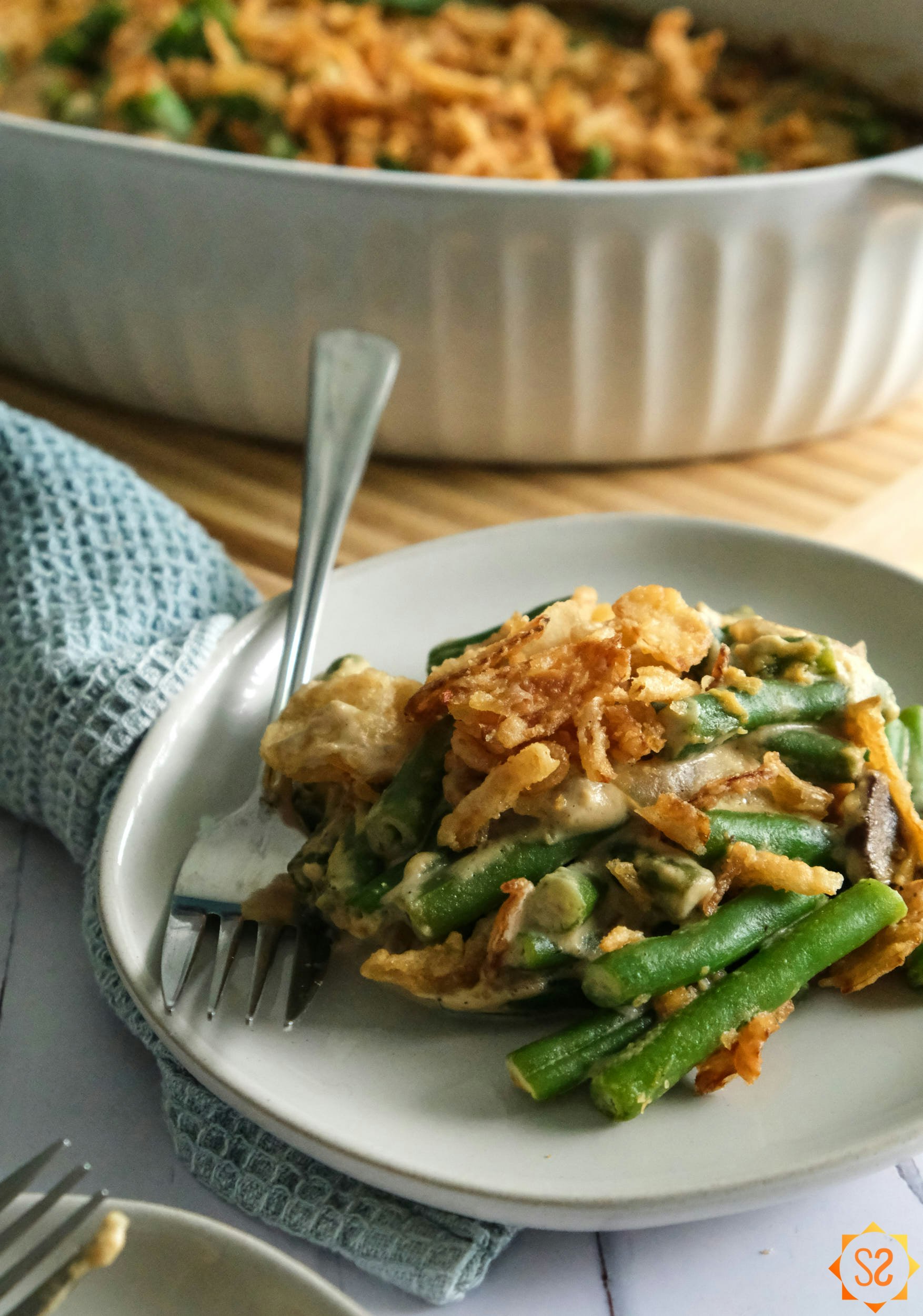 A serving of vegan green bean casserole on a plate, with the whole casserole behind it.