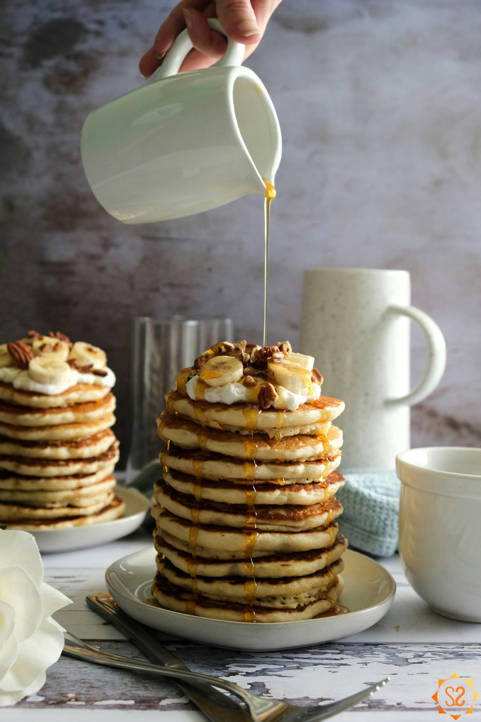 Pouring maple syrup over a stack of vegan buttermilk pancakes