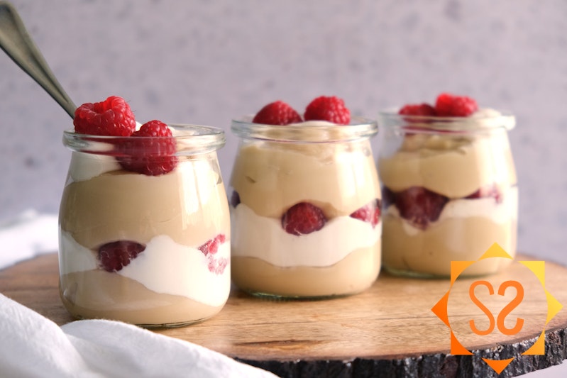 Three jars of vegan vanilla pudding on wooden slab with whipped cream and raspberries
