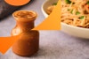 A jar of peanut sauce with a bowl of noodles in the background