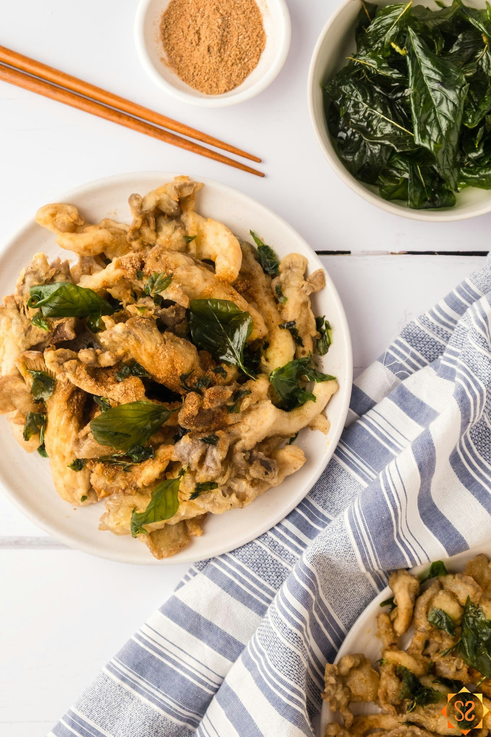 Fried oyster mushrooms on two plates with fried basil, seasoning powder, and chopsticks.