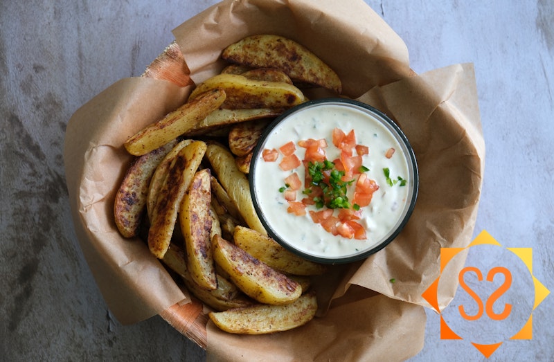 Top-down view of potato wedges in a large wooden bowl with jalapeño dip 
