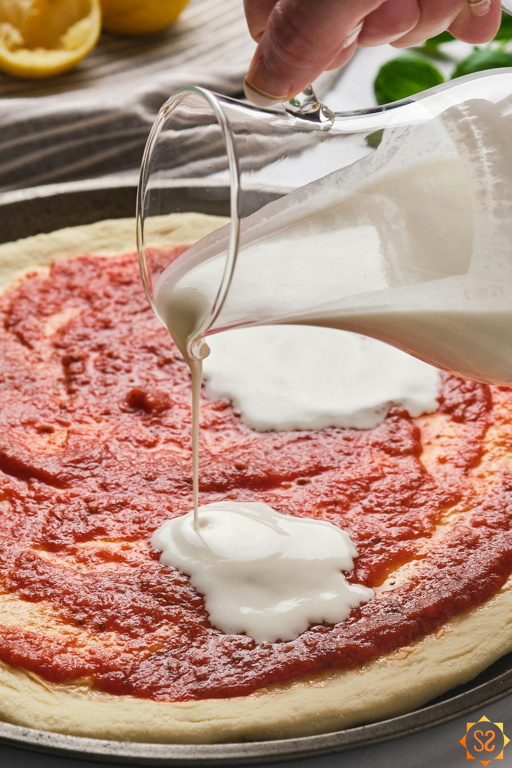 Vegan liquid pizza mozzarella being poured from a pitcher onto an unbaked pizza.