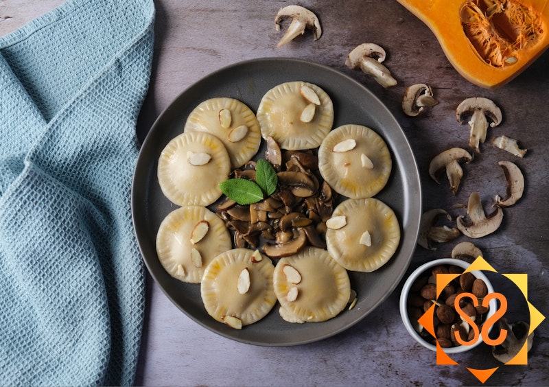 Vegan butternut squash ravioli on a plate with mushrooms, squash, and almonds nearby