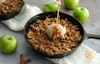 Pouring caramel sauce on top of a skillet of apple crisp with a scoop of vegan vanilla ice cream.