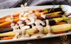 A close-up view of roasted carrots on a platter topped with cashew-tahini sauce and almond slices
