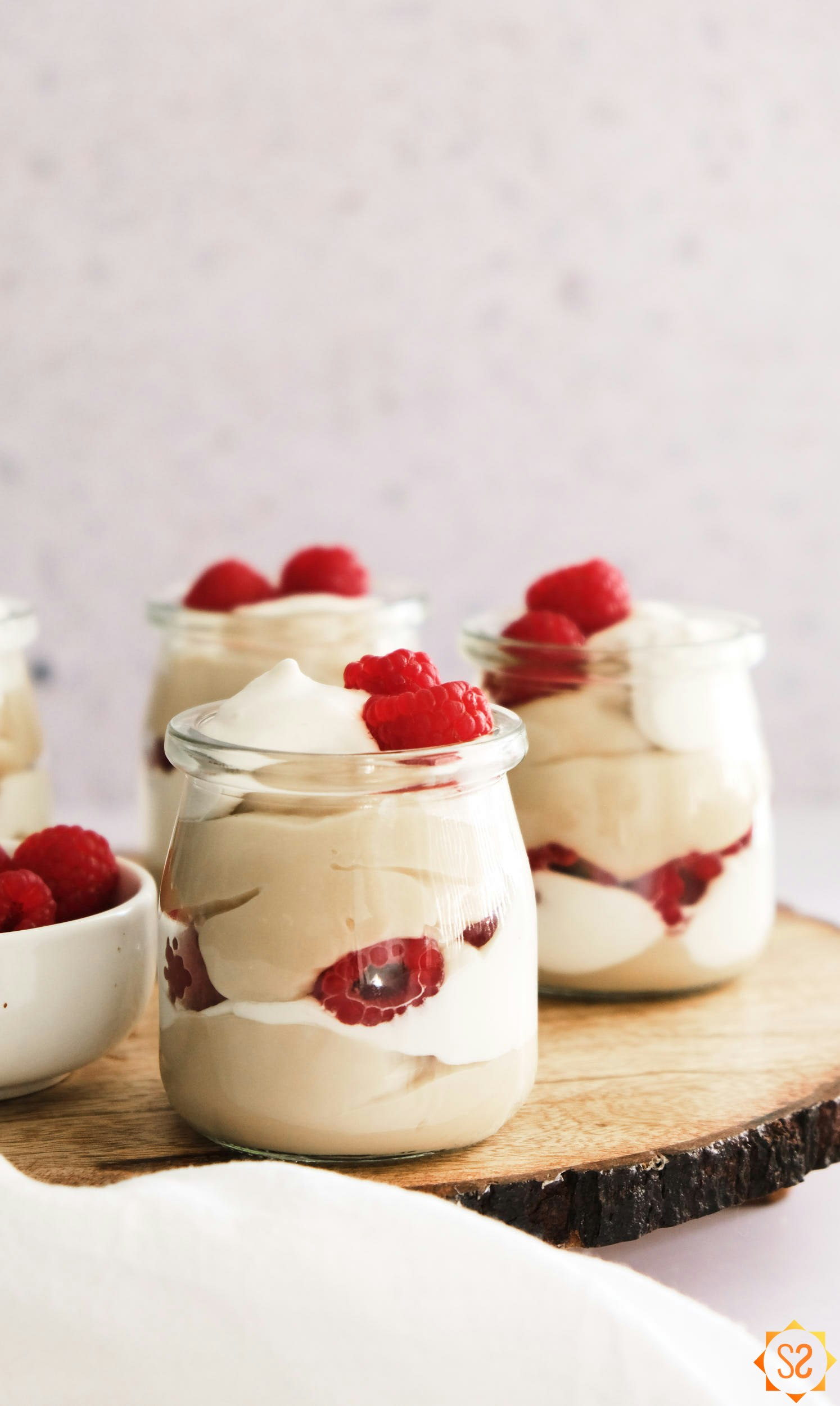 Vegan vanilla pudding in jars on wooden slab with raspberries and whipped cream