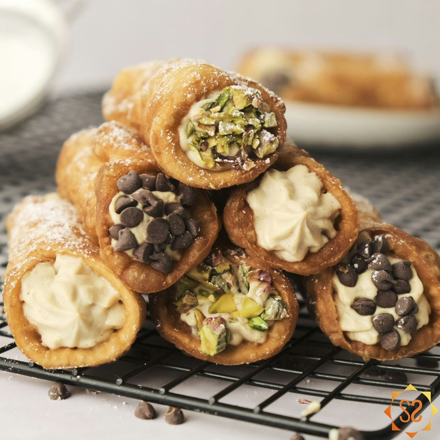 Vegan cannoli stacked on a cooling rack, some with chocolate chips on the ends, others with pistachios.