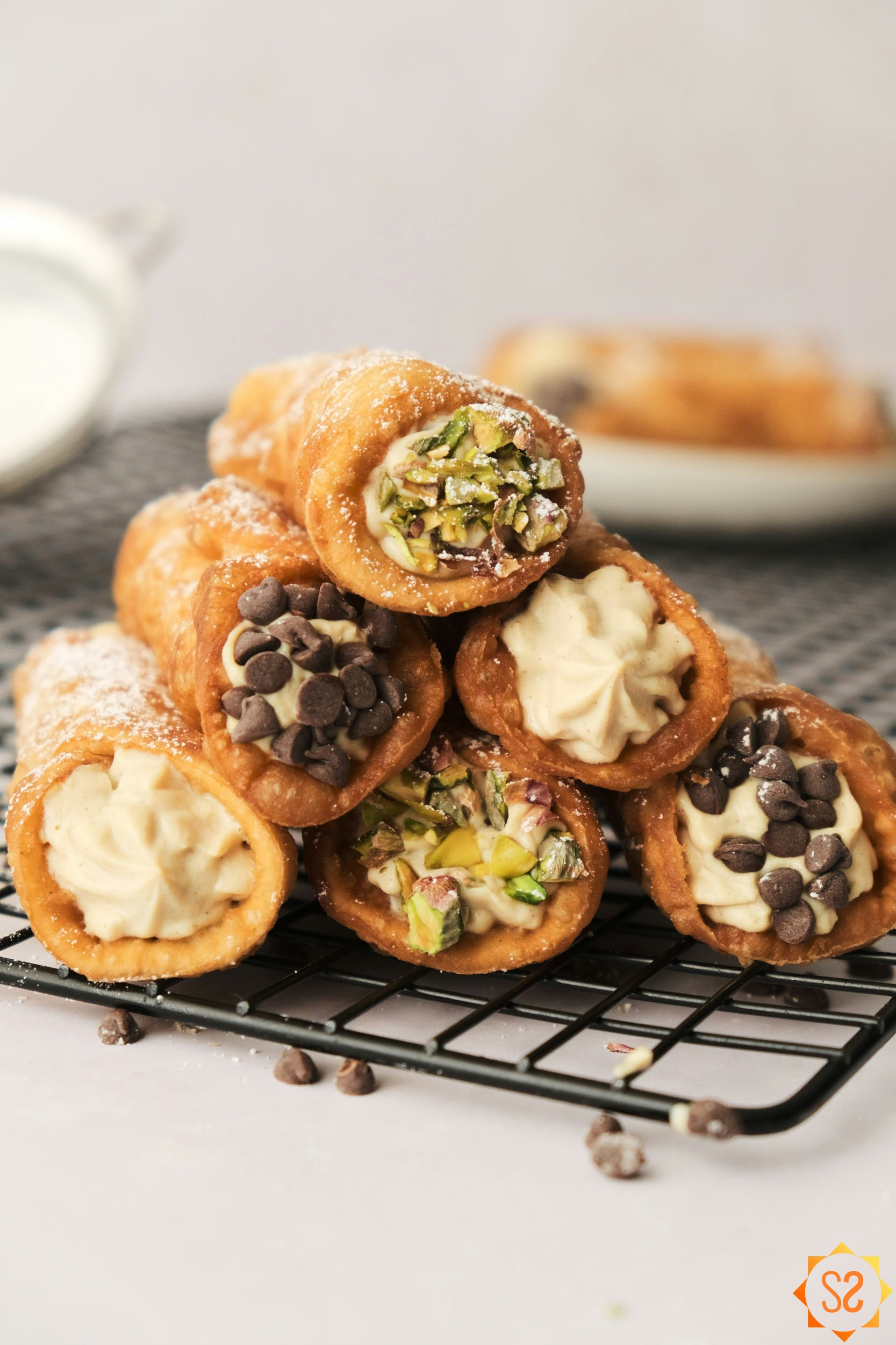 Vegan cannoli stacked on a cooling rack, some with chocolate chips on the ends, others with pistachios