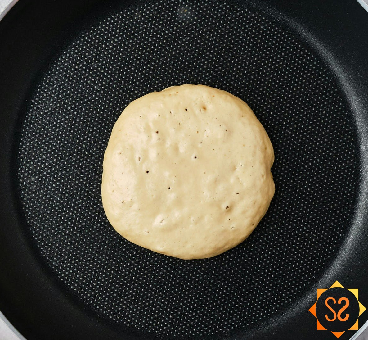 A vegan protein pancake in a pan, ready to be flipped, with bubbles in the center.