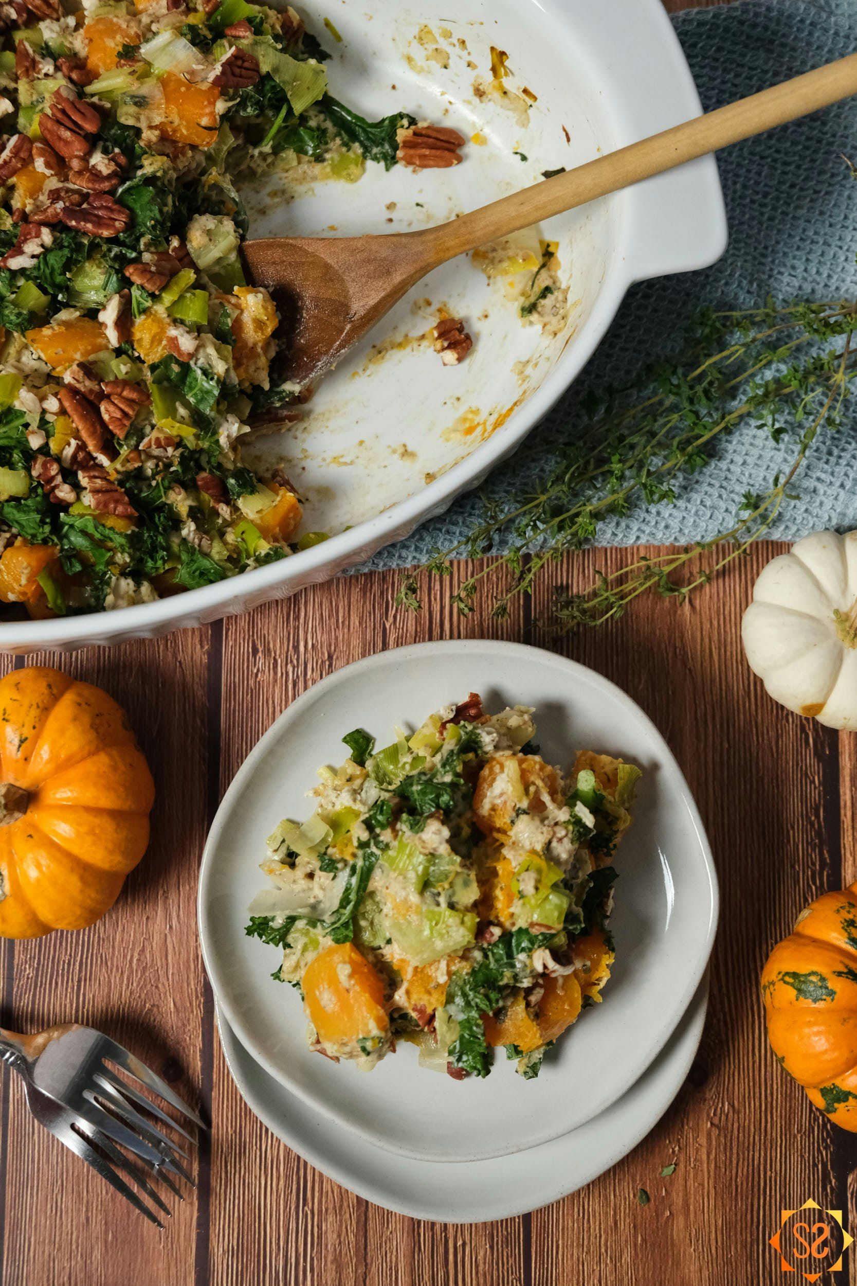 butternut squash casserole in a dish with a wooden spoon, with a plate of squash, plus pumpkins and thyme sprigs.