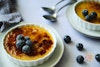 a close-up view of vegan creme brulee dish with blueberries; a second dish and spoons are in the background