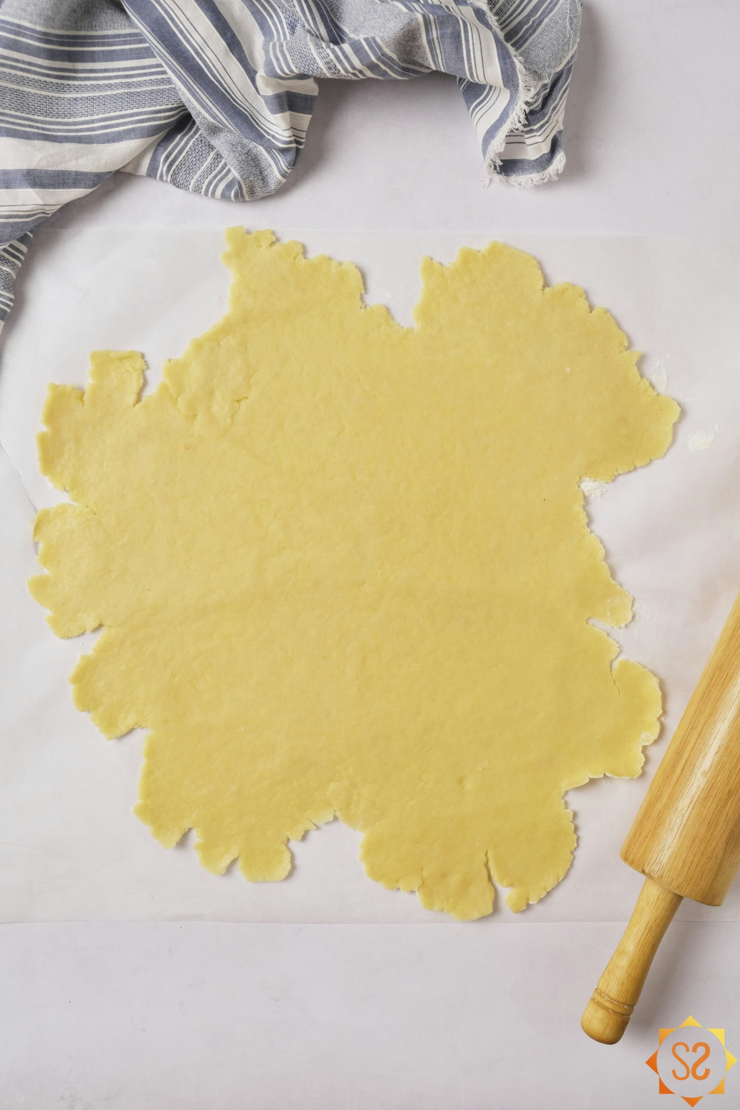 Pate brisee dough rolled out on a piece of parchment paper with a rolling pin to the side.
