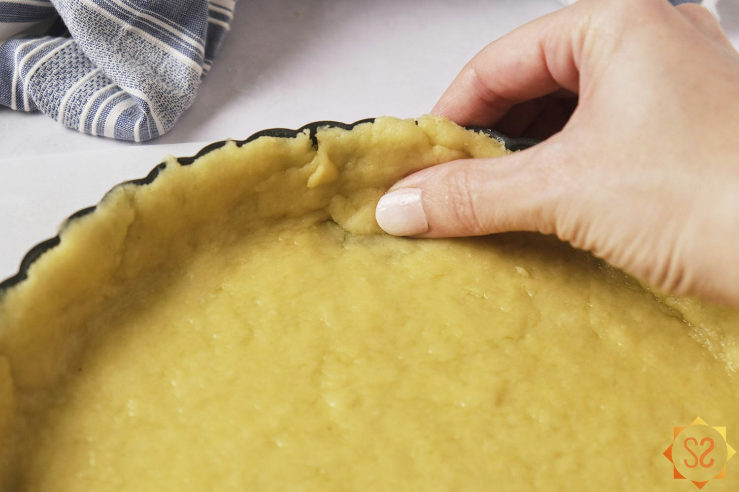 A hand pressing a piece of dough into a part of the crust that requires a patch.