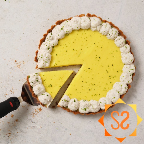 A top-down view of a vegan key lime pie with one slice being pulled out by a pie server.