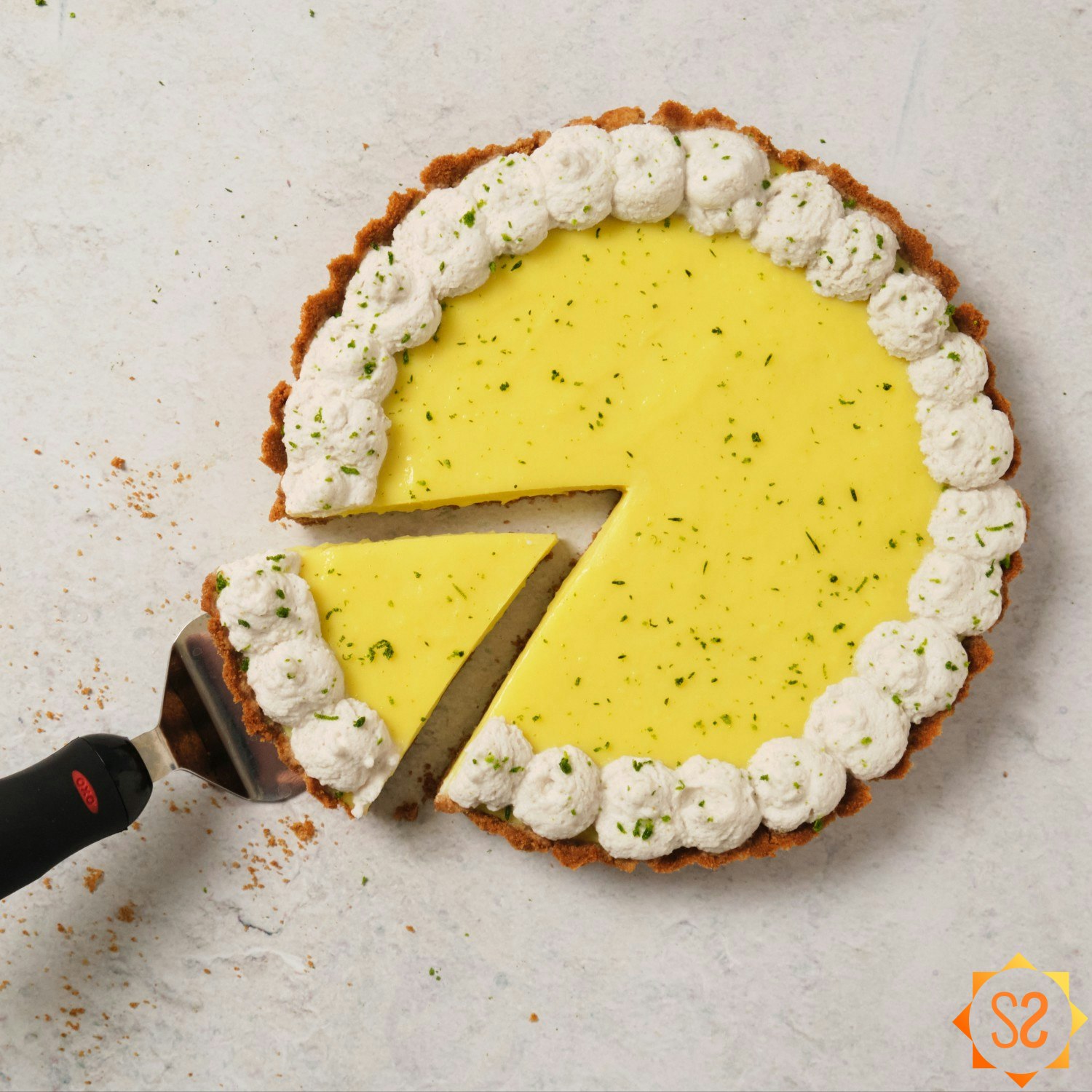 A top-down view of a vegan key lime pie with one slice being pulled out by a pie server.