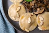 A close-up view of three butternut squash ravioli on a plate, topped with almonds, and mushrooms on the side
