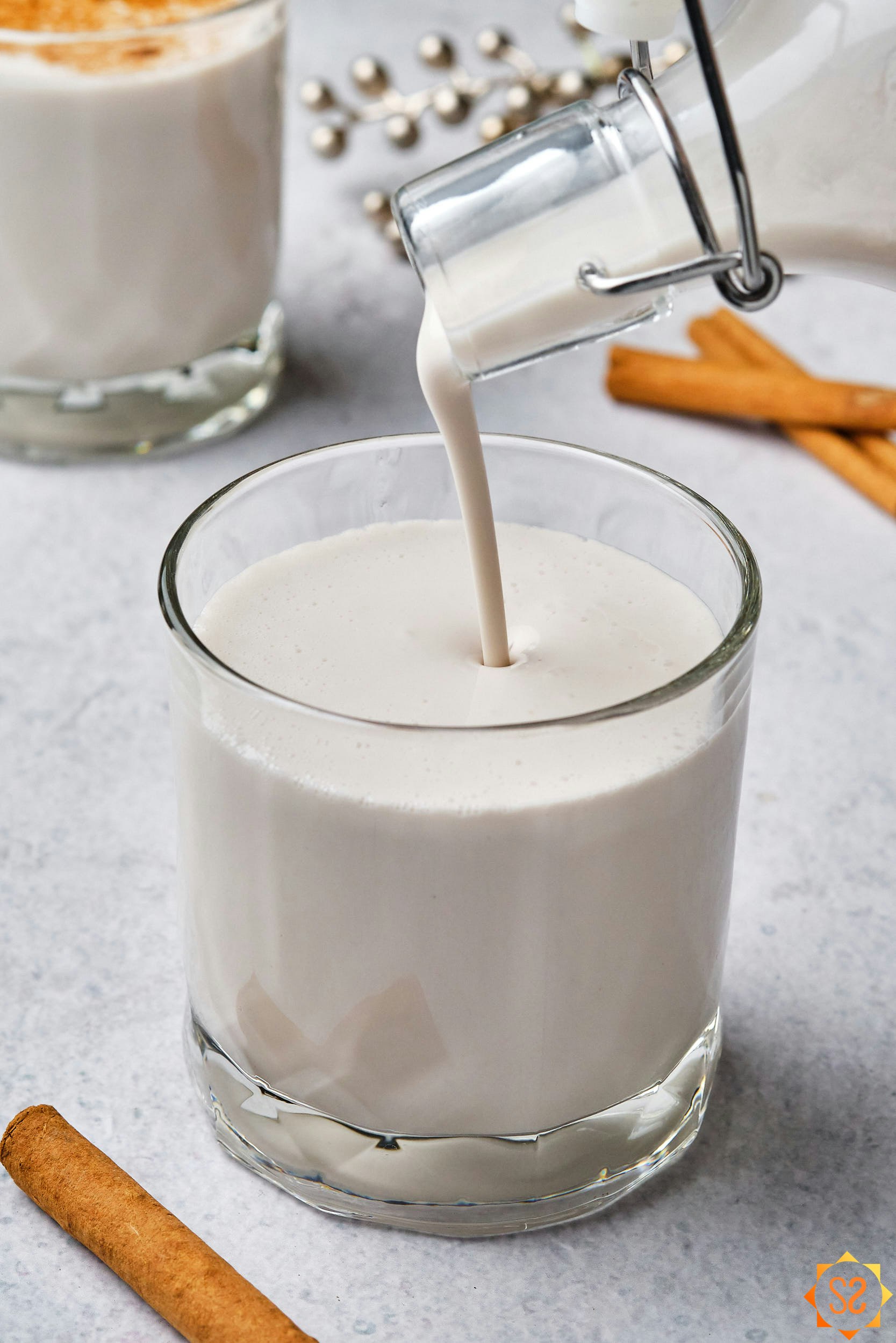 Vegan coquito being poured from a glass bottle into a glass.