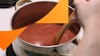 Pizza sauce in a saucepan with a hand using a wooden spoon to stir it