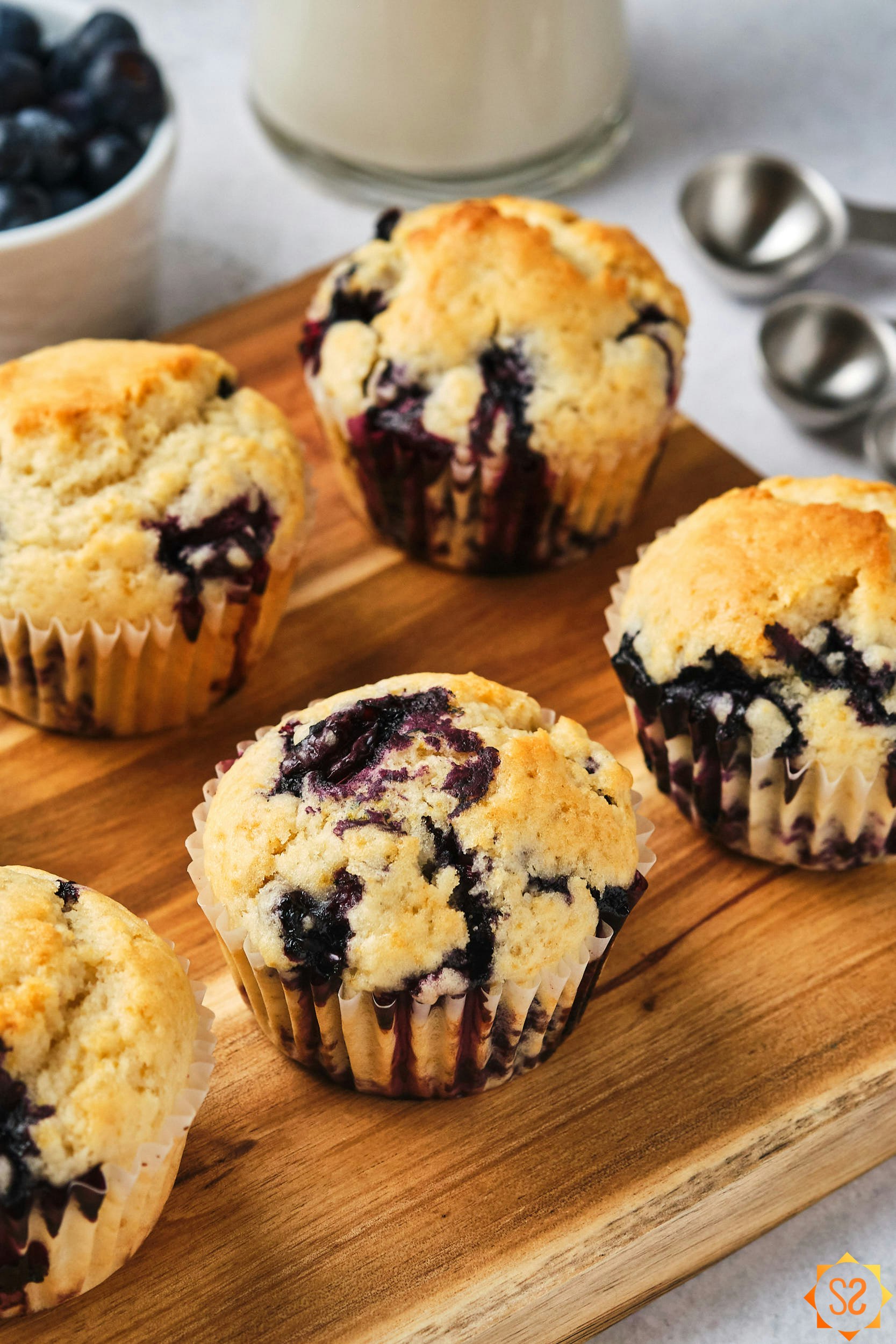 Vegan blueberry muffins on a wood serving board, with almond milk and blueberries in the background.