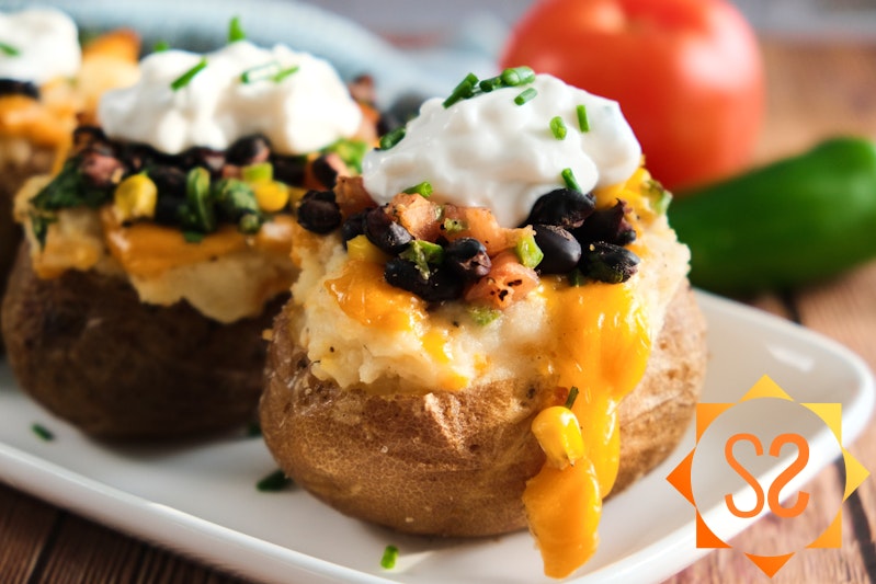 Vegan Tex-Mex baked potatoes on a long plate with a tomato and jalapeno in the background.
