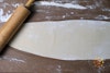 One sheet of ravioli dough rolled out on a floured parchment paper surface, with a rolling pin to the left.