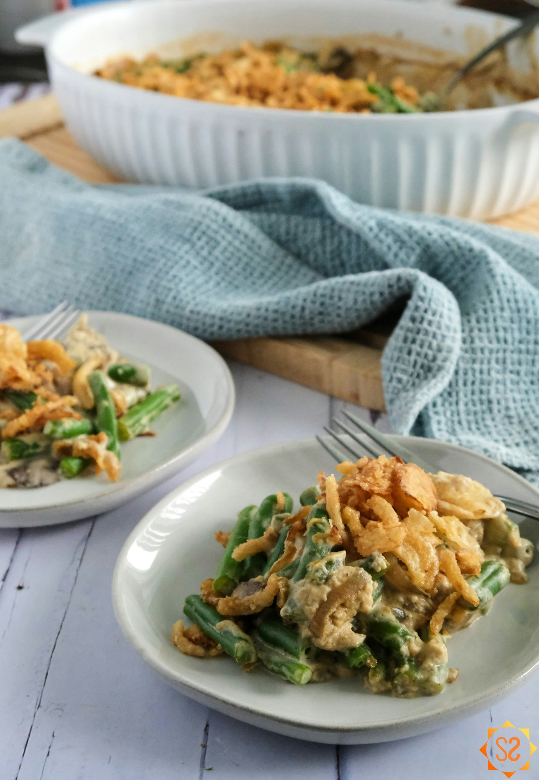 Two plates of green bean casserole with the casserole dish behind in the background
