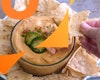 A hand dipping a tortilla chip into vegan queso