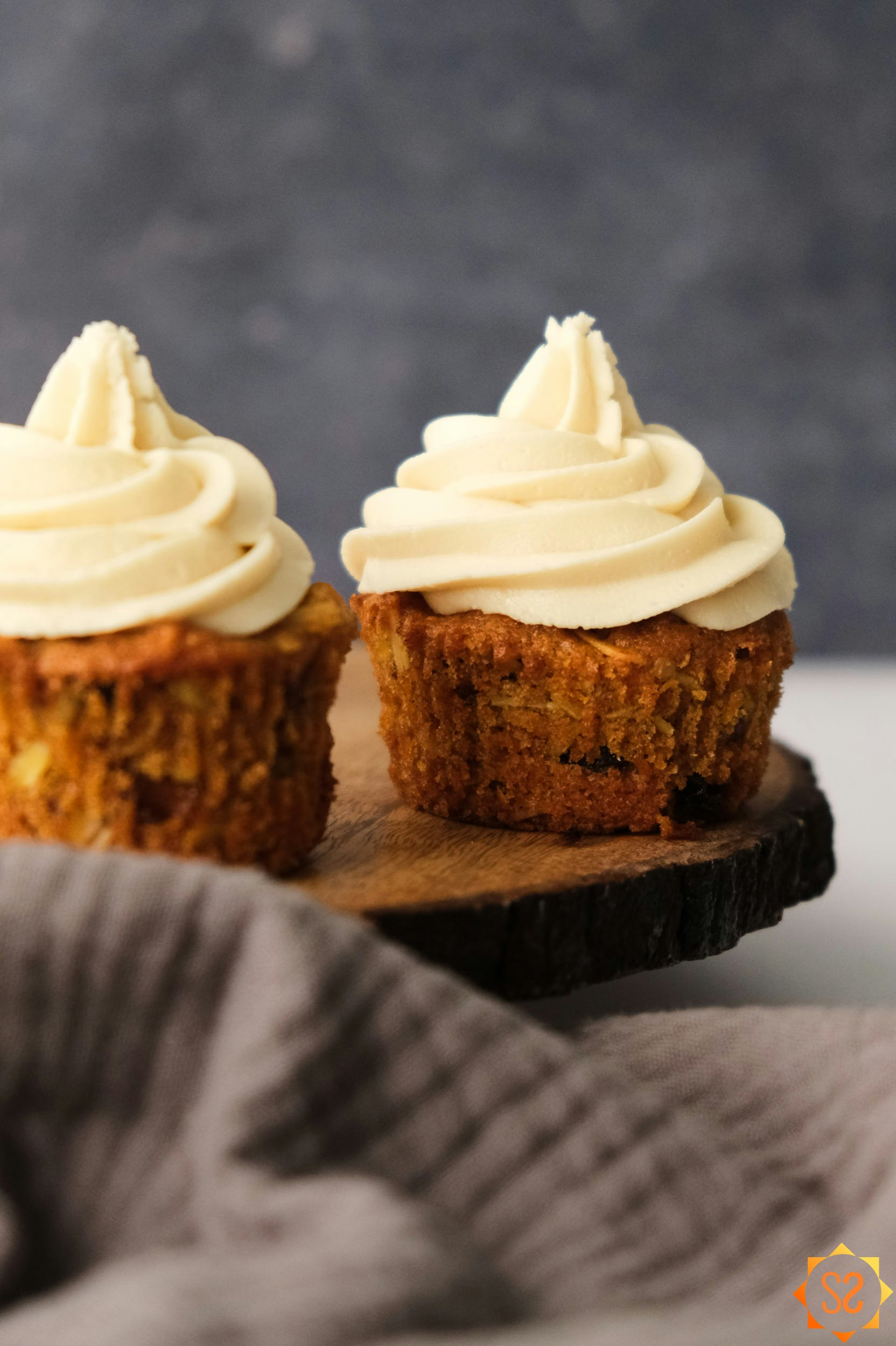 two vegan carrot cake cupcakes on a wooden platter