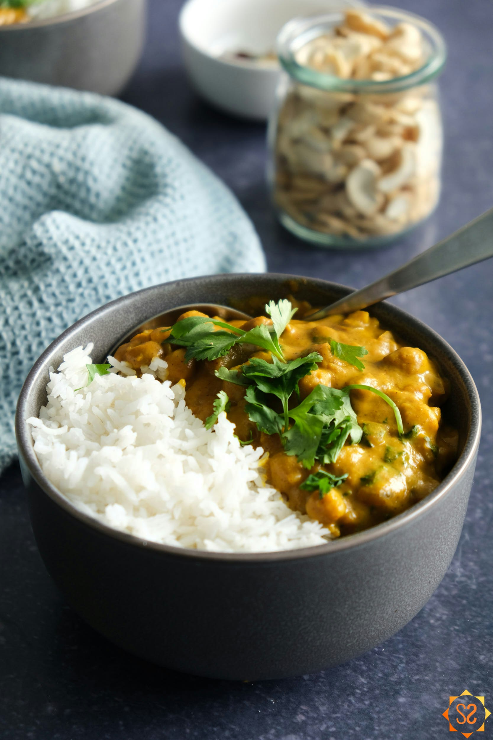 Chickpea Curry in bowl with rice and cashews behind