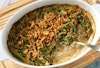 Green bean casserole in a casserole dish with a spoon, some of the casserole has been scooped out