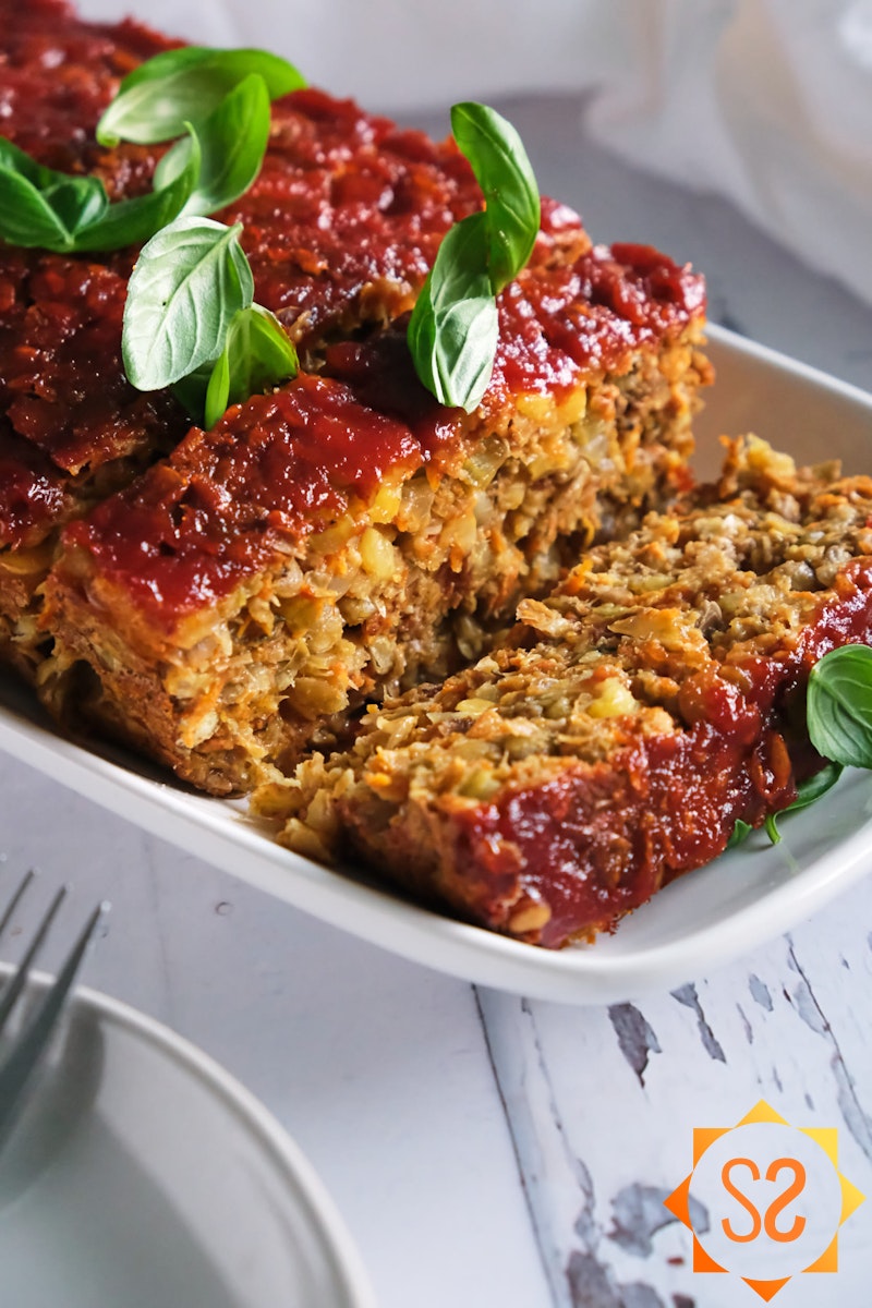 a close view of a sliced lentil loaf topped with basil, plates and forks in the foreground