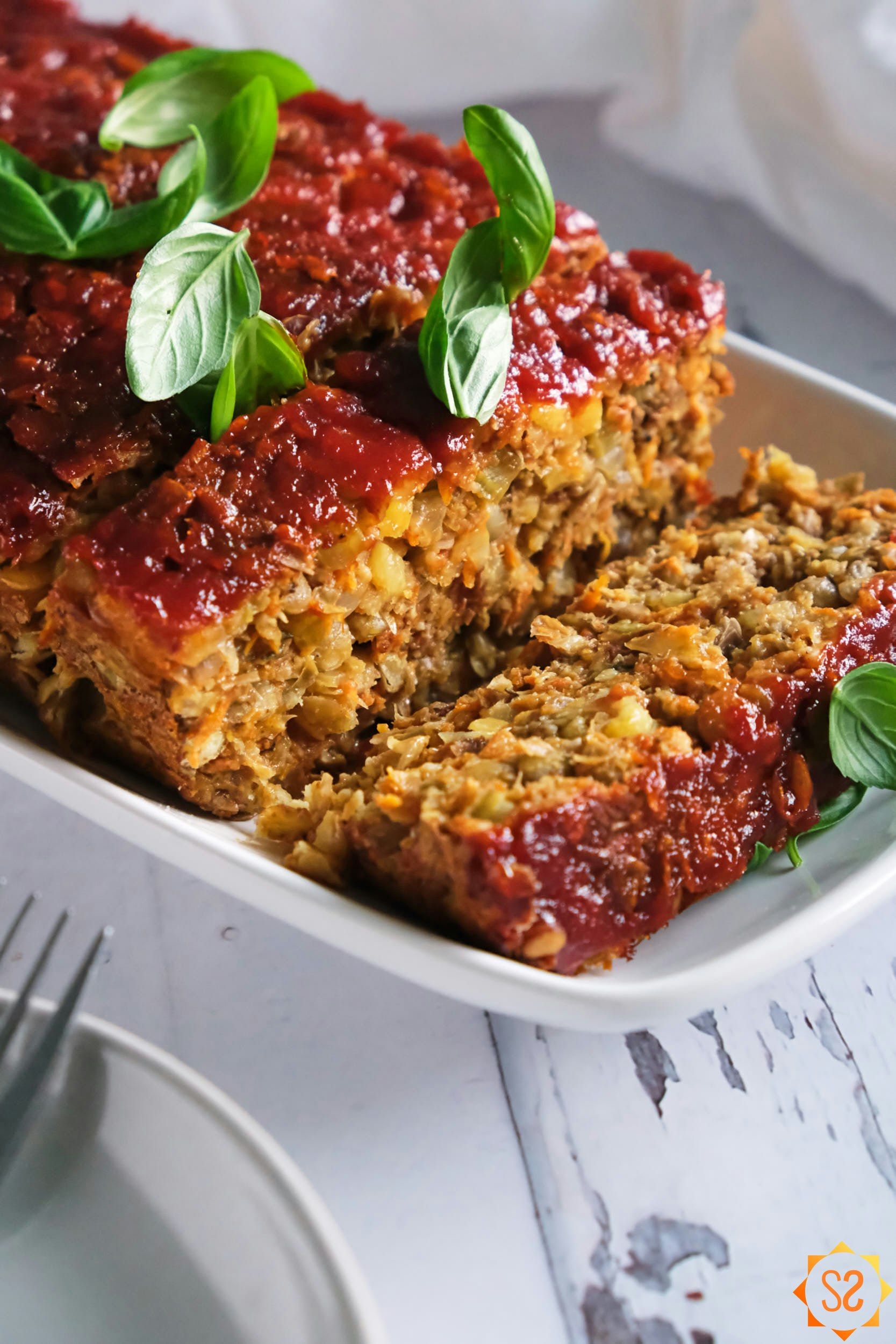 a close view of a sliced lentil loaf topped with basil, plates and forks in the foreground