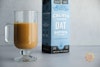 Califia Farms Oat Barista Blend mixed with coffee in a mug, with the container behind it to the right.