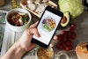 A phone showing an Instagram photo of a food bowl, in front of a bunch of ingredients on a counter