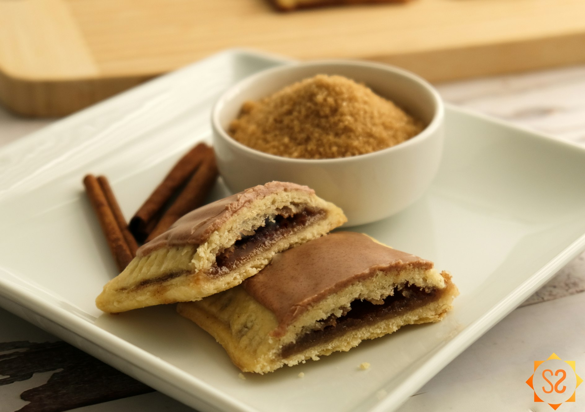 Homemade brown sugar and cinnamon Pop-tart on a plate with a dish of brown sugar and cinnamon sticks behind it