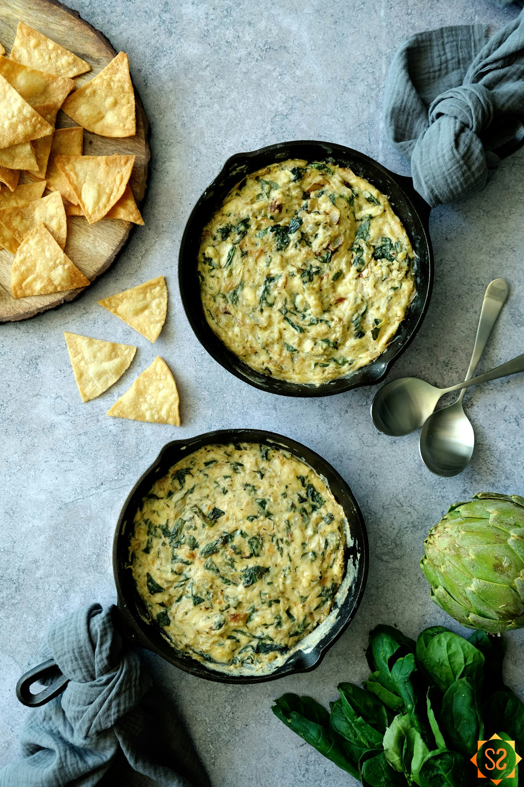 vegan spinach and artichoke dip in skillets with chips and spoons