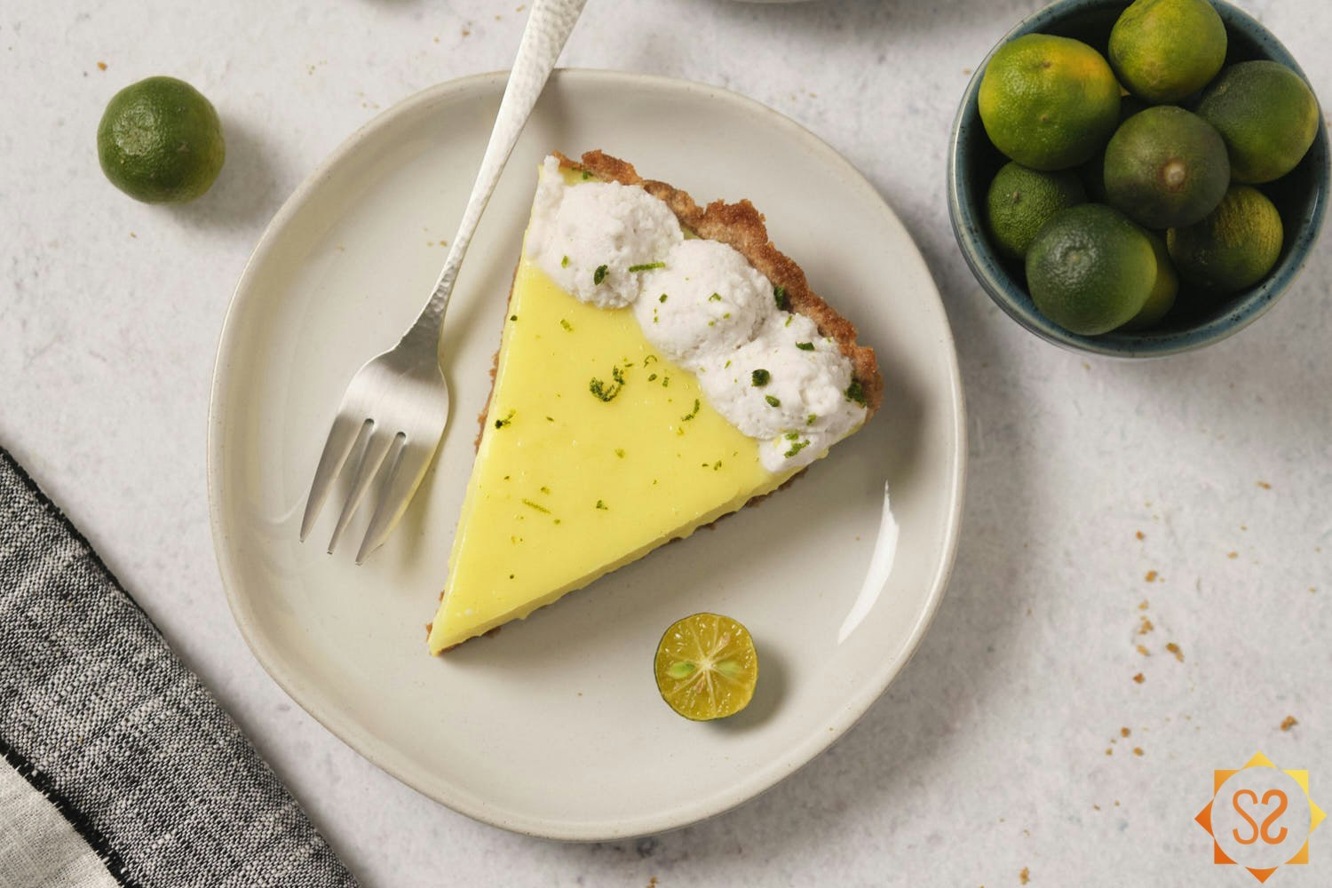 A slice of vegan Key lime pie on a plate topped with Nature's Charm coconut whipped cream and Key lime zest.