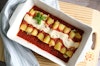 top-down view of vegan cannelloni in a casserole dish, on top of a cutting board, with a kitchen towel to the side