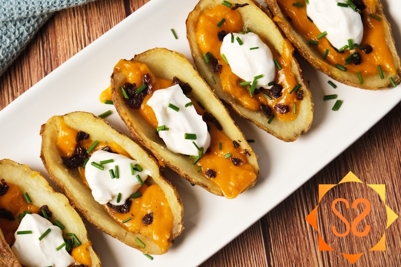 A top-down view of vegan potato skins on a platter with vegan cheddar, sun-dried tomatoes, vegan sour cream, and chives.