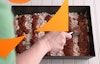 Hands using a spoon to spread sauce across the top of the pizza.