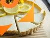 A lemon tart on a cutting board, with two slices sliced.