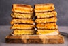 Five different grilled cheeses with five vegan cheeses, stacked on a serving board