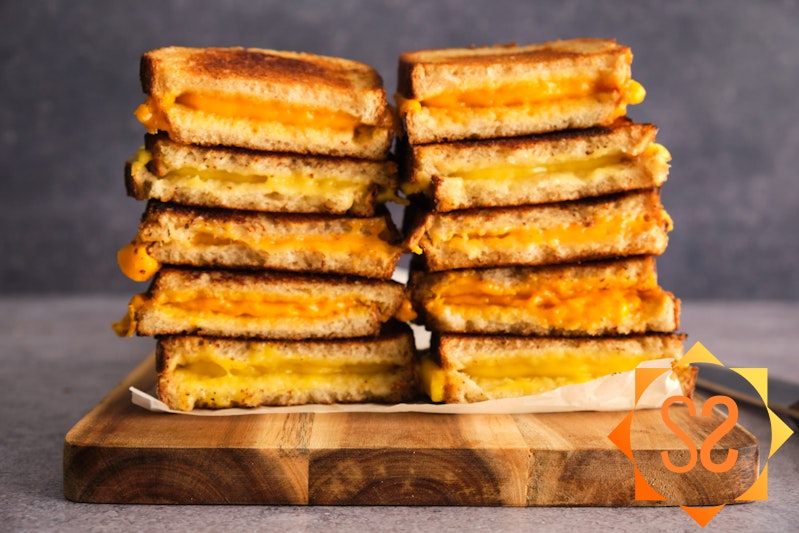 Five different grilled cheeses with five vegan cheeses, stacked on a serving board