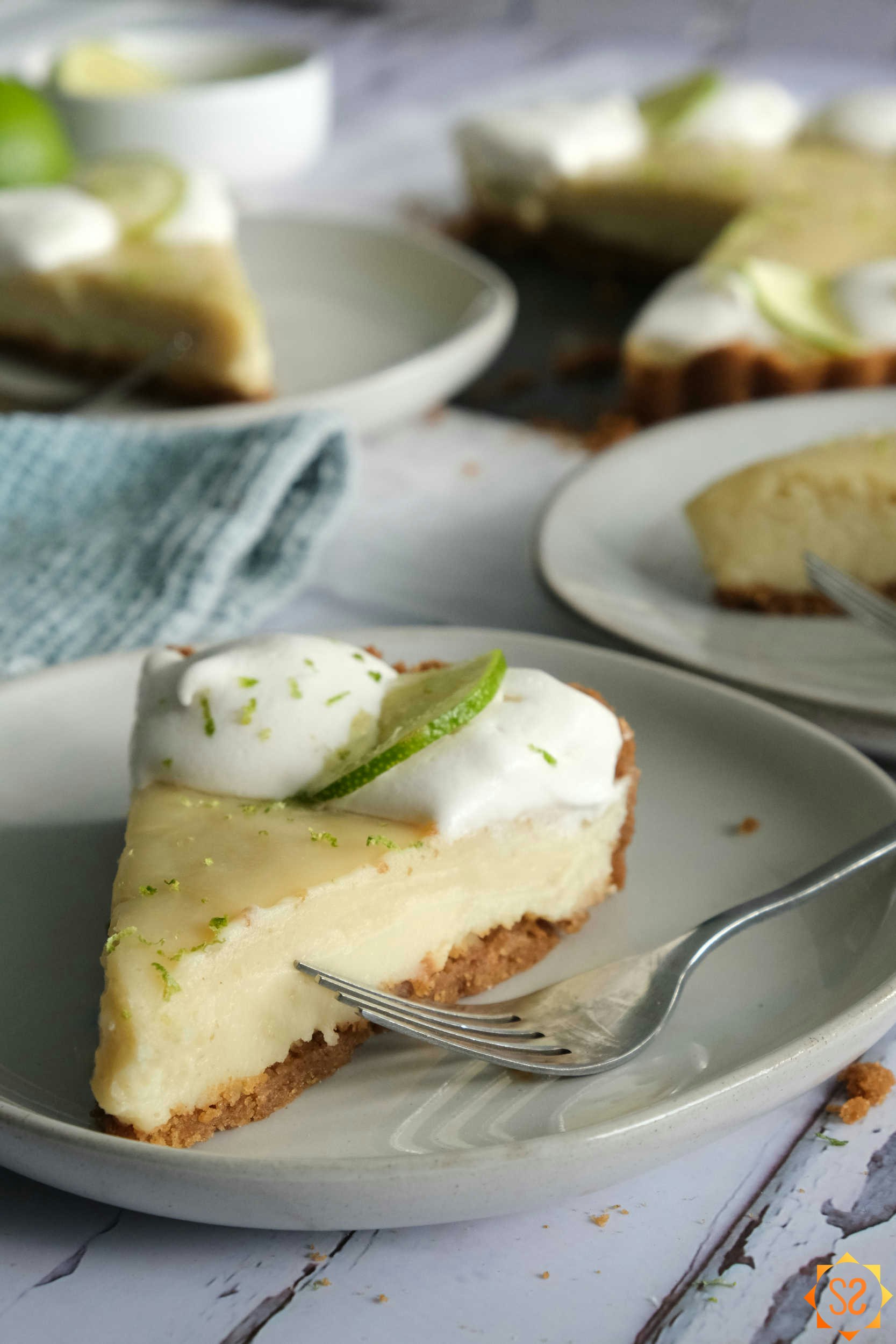 A Key lime pie slice on a plate with the whole pie and more slices in the background