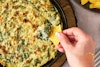 A hand dipping a tortilla chip into a pan of vegan spinach and artichoke dip.
